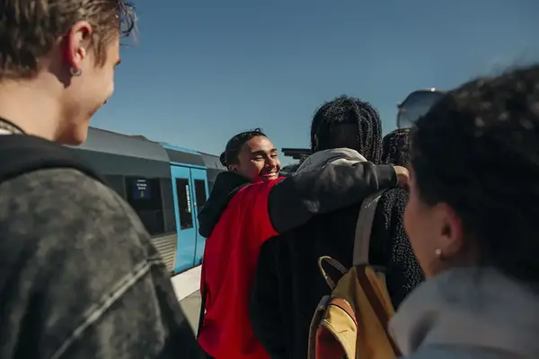 Ungdomar med utländsk bakgrund håller om varandra och ler på en tågstation.