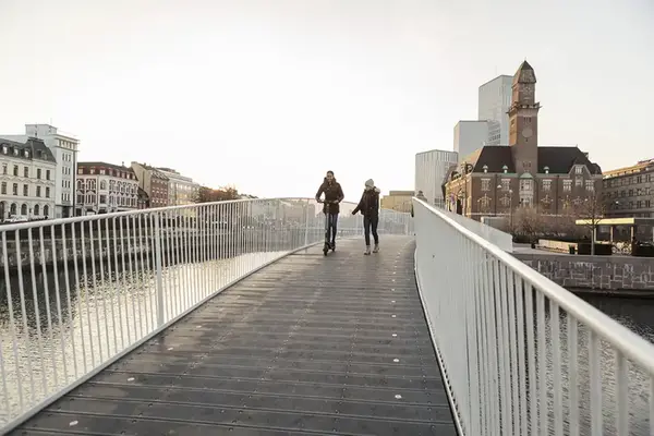 Två flickor åker sparkcykel respektive går över en gångbro.