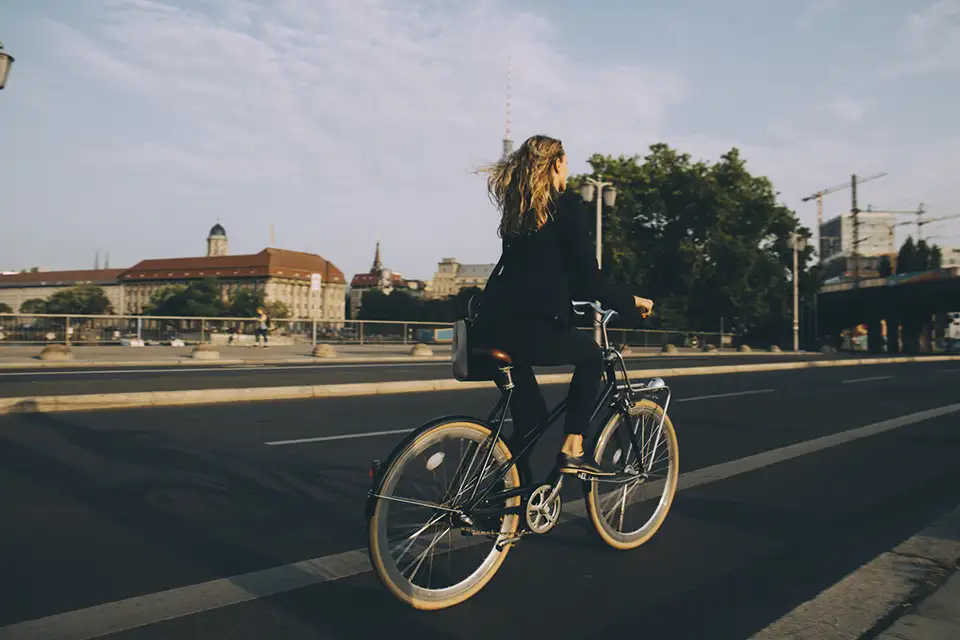 En kvinna i svart kavaj cyklar över en bro i en stad.